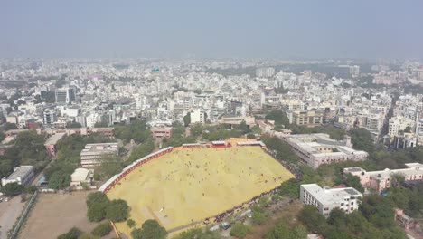 Rajkot-Kite-Festival-Luftaufnahme-Einer-Drohne-Es-Gibt-Ein-Großes-Feld-Umgeben-Von-Büschen,-Wo-Viele-Touristen-Verschiedene-Drachen-Vom-Feld-Steigen-Lassen