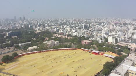 Vista-Aérea-Del-Festival-De-Cometas-De-Rajkot,-Hay-Muchas-Cometas-Grandes-Volando-En-La-Cámara-Del-Dron-Y-También-Hay-Muchas-Casas-Residenciales-Alrededor