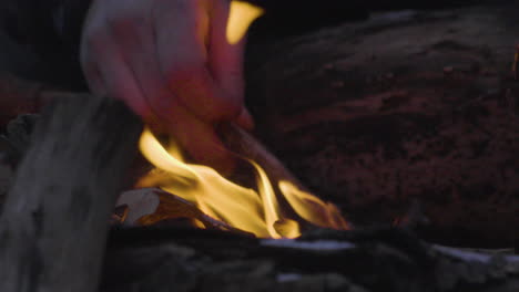 Nahaufnahme-Einer-Männerhand,-Die-Einen-Kleinen-Stock-Hält,-Mit-Dem-Er-Ein-Kleines-Lagerfeuer-Schürt