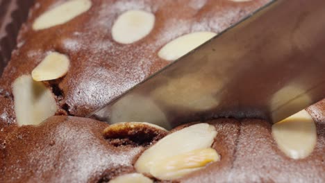 Metal-knife-cuts-through-chocolate-and-almond-cake,-extreme-close-up