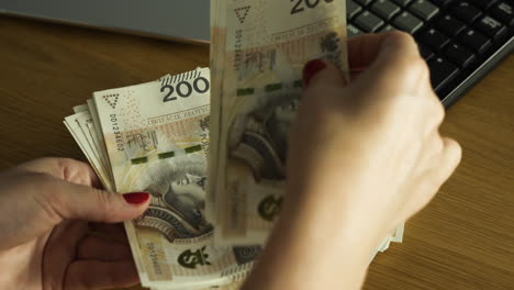 Female-hands-counting-200-Polish-zloty-bills-at-the-table-with-calculator-in-the-background---finance,-business,-house-budget-concept,-close-up-shot