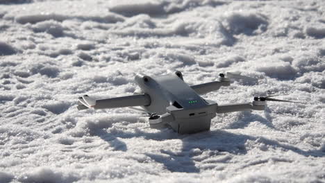 DJI-Mini-Drohne-Auf-Schneebedecktem-Boden-Platziert,-Propeller-Drehen-Sich-Und-Sie-Hebt-Ab