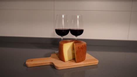 Zoom-out-shot-of-a-big-cutted-cheese-roll-on-cutting-board-and-two-glasses-of-red-wine