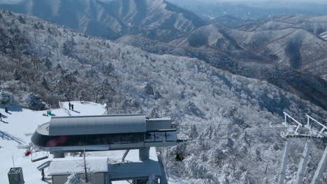 La-Gente-Viaja-En-Telesilla-De-Esquí-En-El-Pico-De-La-Montaña-Balwangsan-Contra-La-Pintoresca-Cordillera-En-La-Estación-De-Esquí-Mona-Yong-Pyong-Pyeongchang-gun,-Gangwon-do,-Corea-Del-Sur---Revelación-Panorámica-En-Cámara-Lenta