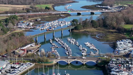 Aerial-shot-flying-over-Hamble-River-boatyard-with-bridges,-boats-and-cars-UK-4K