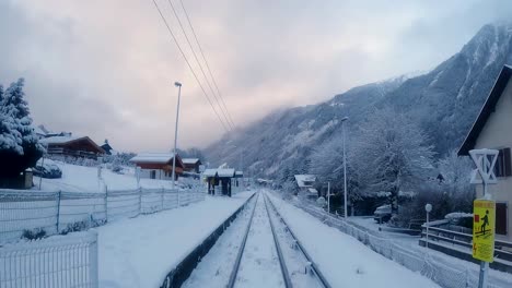 Upwards-pan-shot-of-railway-tracks-in-snowy-scenic-village,-sun-glowing-through-clouds