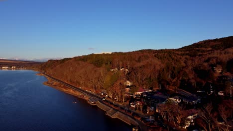 Luftaufnahme-Eines-Ruhigen-Seeufers-Mit-Bahngleisen-Und-Dichtem-Wald-Zur-Goldenen-Stunde