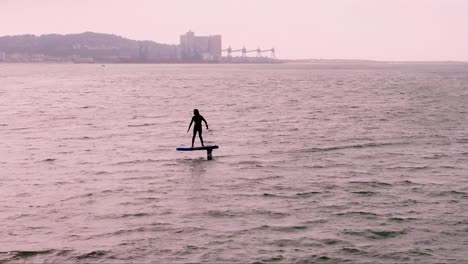 aerial-tracking-of-sportsman-falls-while-practicing-hydrofoil-on-the-Tagus-River,-with-Caparica-in-the-background-in-cloudy-day