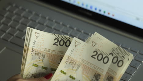 Female-hands-counting-200-Polish-zloty-bills-on-a-laptop---home-budget-concept-close-up-shot