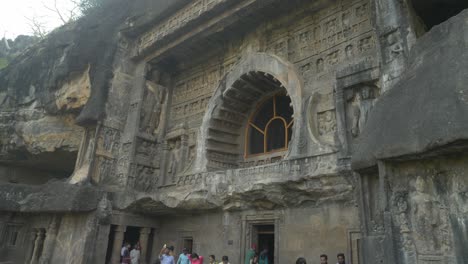 The-crowd-of-tourists-sightseeing-world-heritage-site-Ajanta-caves,-Exterior-wall-carvings-of-Lord-Buddha-and-entrance-to-the-shrine-at-Ajanta-caves