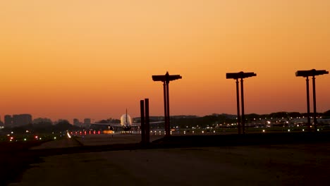 Airplane-landing-on-runway-at-dusk-with-city-skyline-silhouette,-golden-sky-backdrop