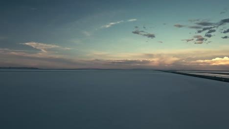 Aerial-view-of-Bonneville-salt-flats-in-Utah-with-the-sun-on-the-horizon-and-sparse-clouds