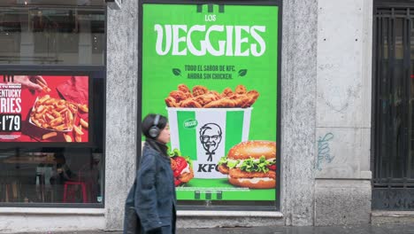 Menschen-Gehen-An-Einer-Straßenwerbung-Von-KFC-Vorbei,-In-Der-Ein-Neues-Vegetarisches-Gericht-Namens-Veggies-Beworben-Wird,-Das-In-Den-Fast-Food-Ketten-Der-Kette-In-Spanien-Erhältlich-Ist