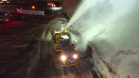 Aerial-View-of-Snowblower-at-Night-Moving-Snow-Taken-From-Streets-of-Montreal,-Canada