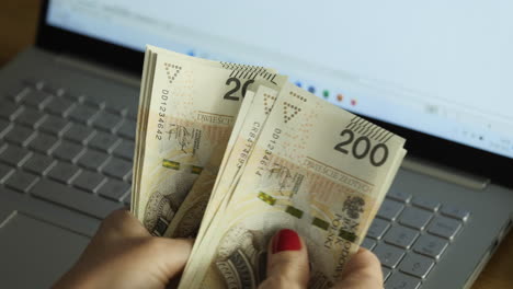 Female-hands-counting-200-Polish-zloty-bills-over-the-laptop---business-or-home-budget-concept,-close-up-shot