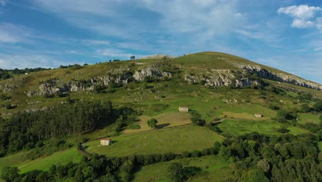 lateral-flight-on-a-white-limestone-mountain-with-green-agricultural-farms-with-their-old-houses-separated-with-trees-and-a-farm-full-of-eucalyptus-trees-on-a-summer-afternoon-Cantabria-Spain