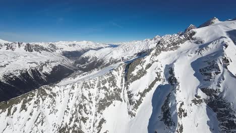 La-Vista-Aérea-Captura-La-Serena-Majestuosidad-De-Las-Montañas-Cubiertas-De-Nieve-Bajo-Un-Cielo-Azul-Claro,-Resaltando-La-Belleza-Intacta-De-Un-Paisaje-Alpino-Invernal.