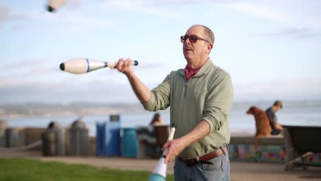 Alter-Mann-Jongliert-Mit-Bowling-Pins-Am-Strand