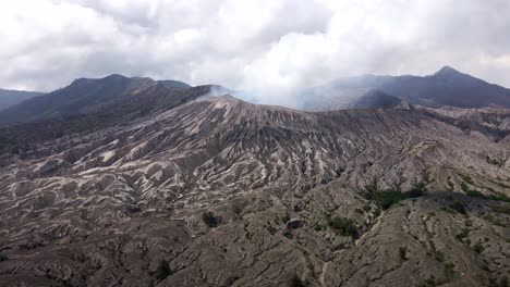 Contempla-El-Majestuoso-Bromo,-Un-Volcán-Icónico-Y-Activo-En-Java-Oriental,-Indonesia,-Que-Muestra-Impresionantes-Actividades-Volcánicas-Mientras-Libera-Oleadas-De-Humo-Gris-Y-Ceniza,-Imágenes-Aéreas-De-Drones-En-4k.