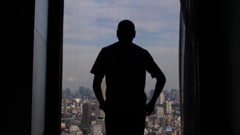 A-man's-silhouette-Walking-towards-Large-Window-In-High-Rise-Building-And-Opening-Curtains-To-Reveal-expansive-city-metropolis-view