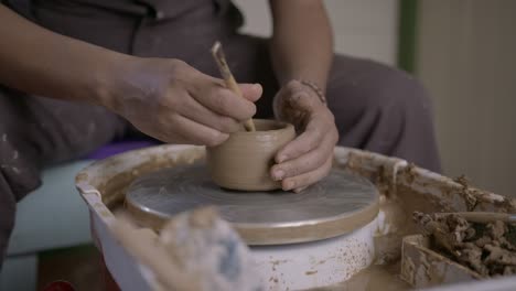 Artisan-shaping-clay-on-a-potter's-wheel-with-tools,-focus-on-hands-and-pottery,-indoor-workshop