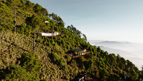 Drone-flying-towards-shanty-houses-near-summit-of-green-inactive-Acatenango-volcano-in-Guatemala-during-sunrise