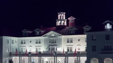 American-flags-displayed-proudly-over-entrance-of-old-white-colonial-style-hotel-at-night