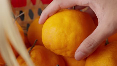 Hand-picks-up-one-of-many-oranges-from-basket,-slomo-close-up