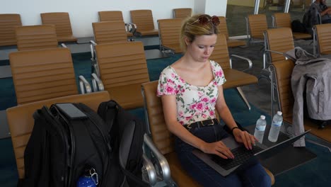 Woman-working-on-laptop-at-airport-waiting-area,-daylight,-casual-attire,-focused-demeanor