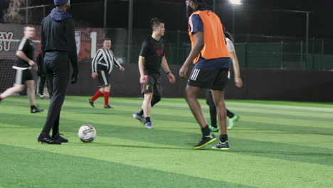 Los-Jugadores-De-Fútbol-Juegan-Al-Aire-Libre-Por-La-Noche-En-Un-Campo-Verde-Iluminado-Con-Césped-Artificial