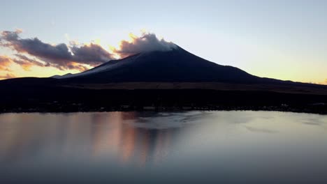 Sunset-silhouette-of-Mount-Fuji-with-reflection-on-lake,-clouds-drifting-by