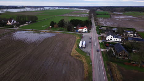 Abgelegene-Straße-Zwischen-Schlammigen-Landwirtschaftlichen-Feldern-Mit-Häusern-Und-Autos-Drohne