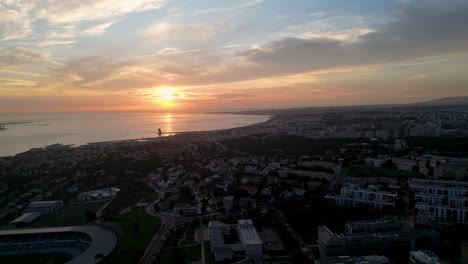 Vista-Por-Drones-Del-Paisaje-Urbano-De-Lisboa-Junto-Al-Mar-Durante-Una-Puesta-De-Sol