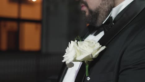 The-groom-preparing-for-his-wedding-at-night,-wearing-a-rose-boutonniere-on-his-black-jacket