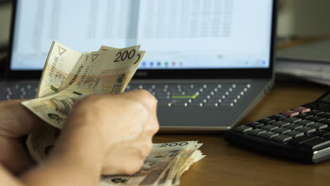 Female-hands-counting-200-Polish-zloty-bills-over-the-laptop-and-calc-sheet---house-budget-concept,-close-up-shot