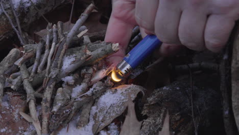 close-up-as-a-man-uses-a-bic-lighter-to-ignite-dried-leaves-and-small-twigs-as-kindling-to-build-a-campfire-in-the-forest-in-winter