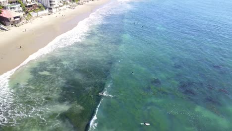 4K-Aerial-View-of-Surfers-in-Laguna-Beach,-California-Riding-Waves-on-a-Warm-Sunny-Day-with-Crystal-Clear-Water-on-the-Pacific-Ocean