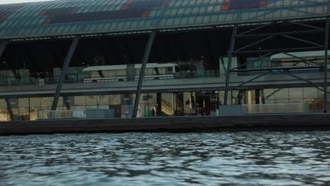 Public-transit-busses-arriving-at-Amsterdam-Central-Station,-view-from-water