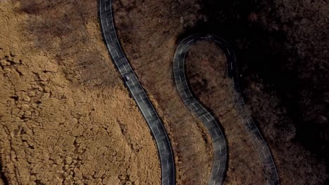Curved-road-slicing-through-barren-landscape,-aerial-view,-minimal-traffic