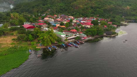 Parking-traditional-boats-at-shore-in-front-of-asian-village-at-Taal-Lake,-Philippines