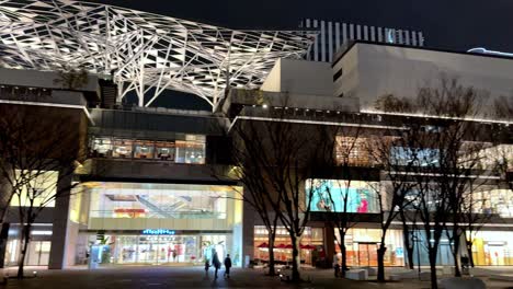 Night-view-of-a-modern-plaza-with-unique-architecture-and-lit-storefronts,-people-walking,-in-Yokohama,-Japan