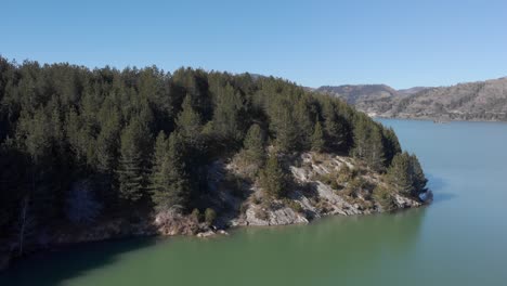 Aerial-over-trees-revealing-mountain-Lake-sunny-day-blue-sky