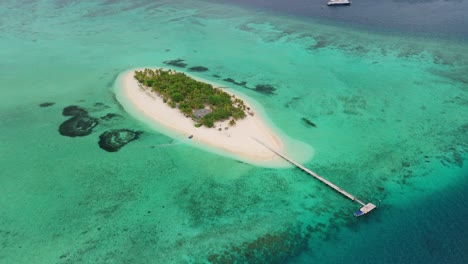 Drone-flying-above-private-island-in-Fiji-with-cruise-ship-in-the-background-as-small-zodiac-tender-arrives-onto-the-beach