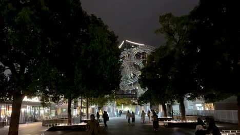 Night-view-of-a-city-park-with-illuminated-art-installation,-people-strolling,-trees-framing-the-scene,-in-Yokohama,-Japan