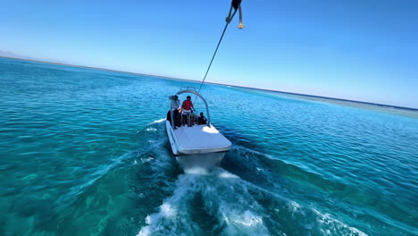 Boat-towing-parasail-over-clear-blue-waters-in-Sharm-El-Sheikh,-Egypt,-vibrant-and-sunny-day,-aerial-view