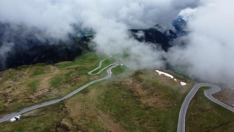 Winding-mountain-road,-surrounded-by-majestic-peaks-and-blanketed-by-swirling-clouds