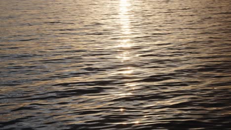 Close-up-of-water-rippling-as-camera-pans-up-towards-sun-and-island-silhouette's