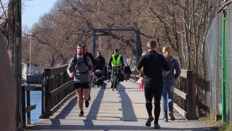 People-walk,-run-and-bicycle-on-wooden-bridge-on-sunny-day-in-Stockholm