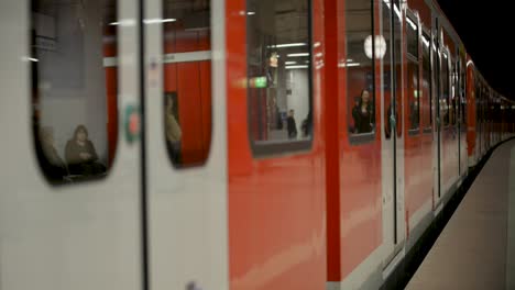 Pasajeros-Visibles-A-Través-De-Las-Ventanas-De-Un-Tren-Rojo-Parado-En-Una-Plataforma-En-Stuttgart,-Ambiente-Nocturno