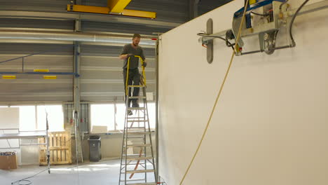 Office-Worker-Climbs-Ladder-to-attach-Side-Panel-of-Truck-With-Ratchet-Strap,-Drone-Shot